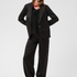 Women modelling a black sateen suit with a black blouse and black kitten heels photographed against a light background.