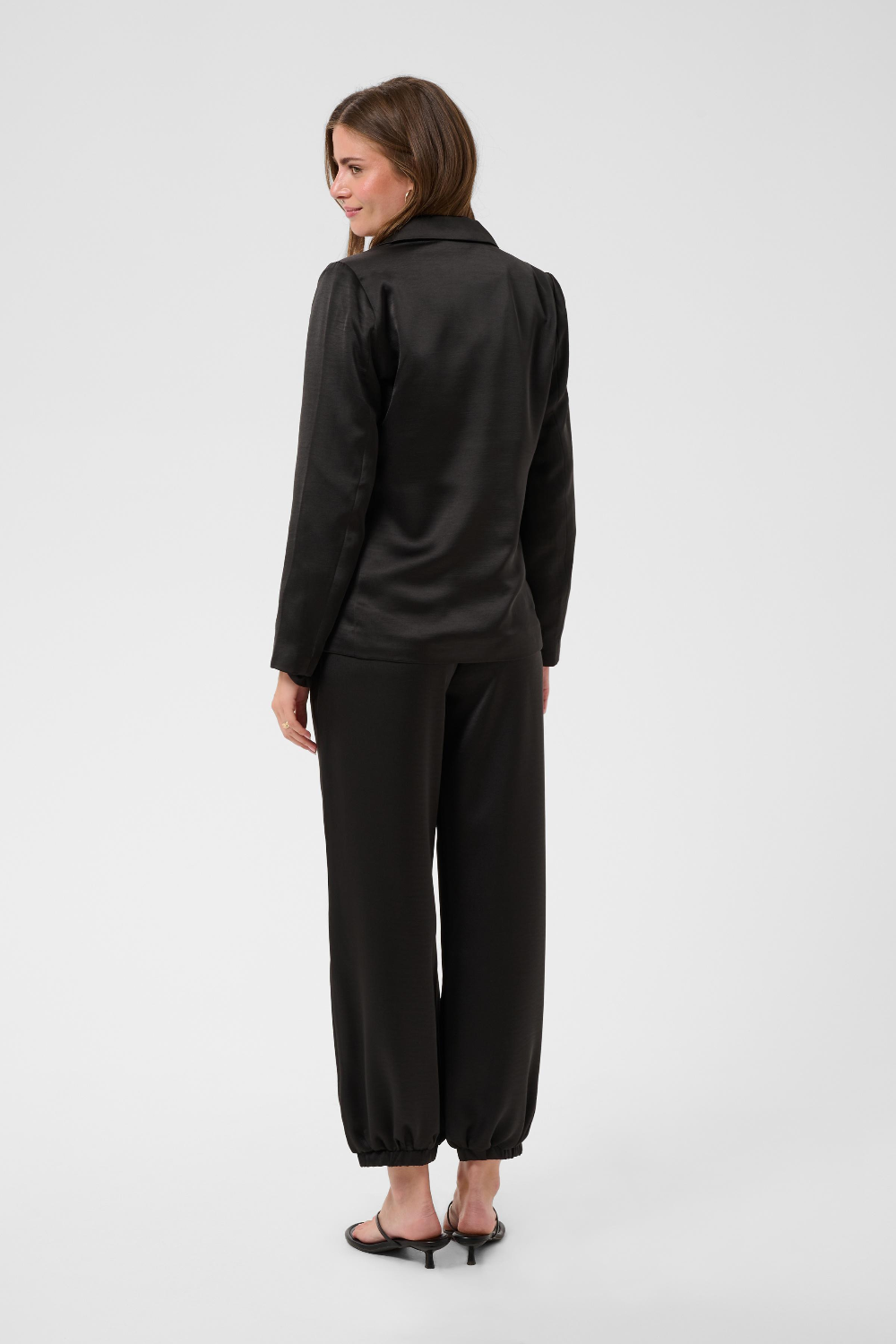 Women, shown from behind, modelling a black sateen suit with black kitten heels photographed against a light background.