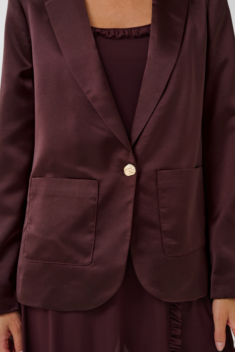 Close up of a woman modelling a deep wine coloured sateen blazer with a matching top and pant photographed against a light background.