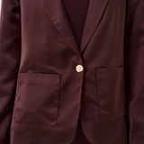 Close up of a woman modelling a deep wine coloured sateen blazer with a matching top and pant photographed against a light background.
