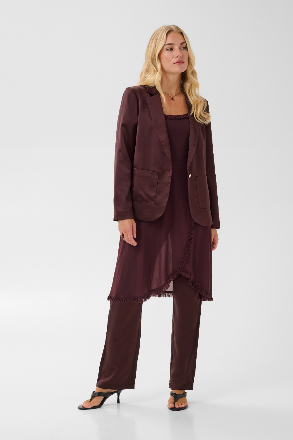 Woman modelling a deep wine coloured sateen blazer with a matching top and pant, and black kitten heels, photographed against a light background.