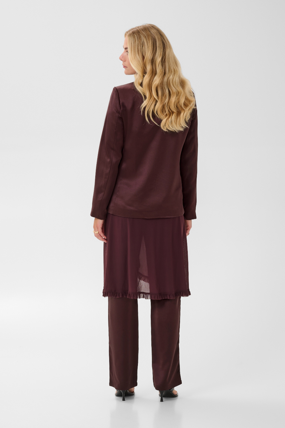 Woman, shown from behind, modelling a deep wine coloured sateen blazer with a matching top and pant, and black kitten heels, photographed against a light background.