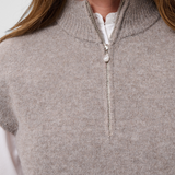 Close up of a woman modelling a brown half zip knit vest with a white shirt against a light backdrop.