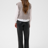Woman, shown from the back, modelling a brown half zip knit vest with a white shirt and black pants black kitten heels against a light backdrop.