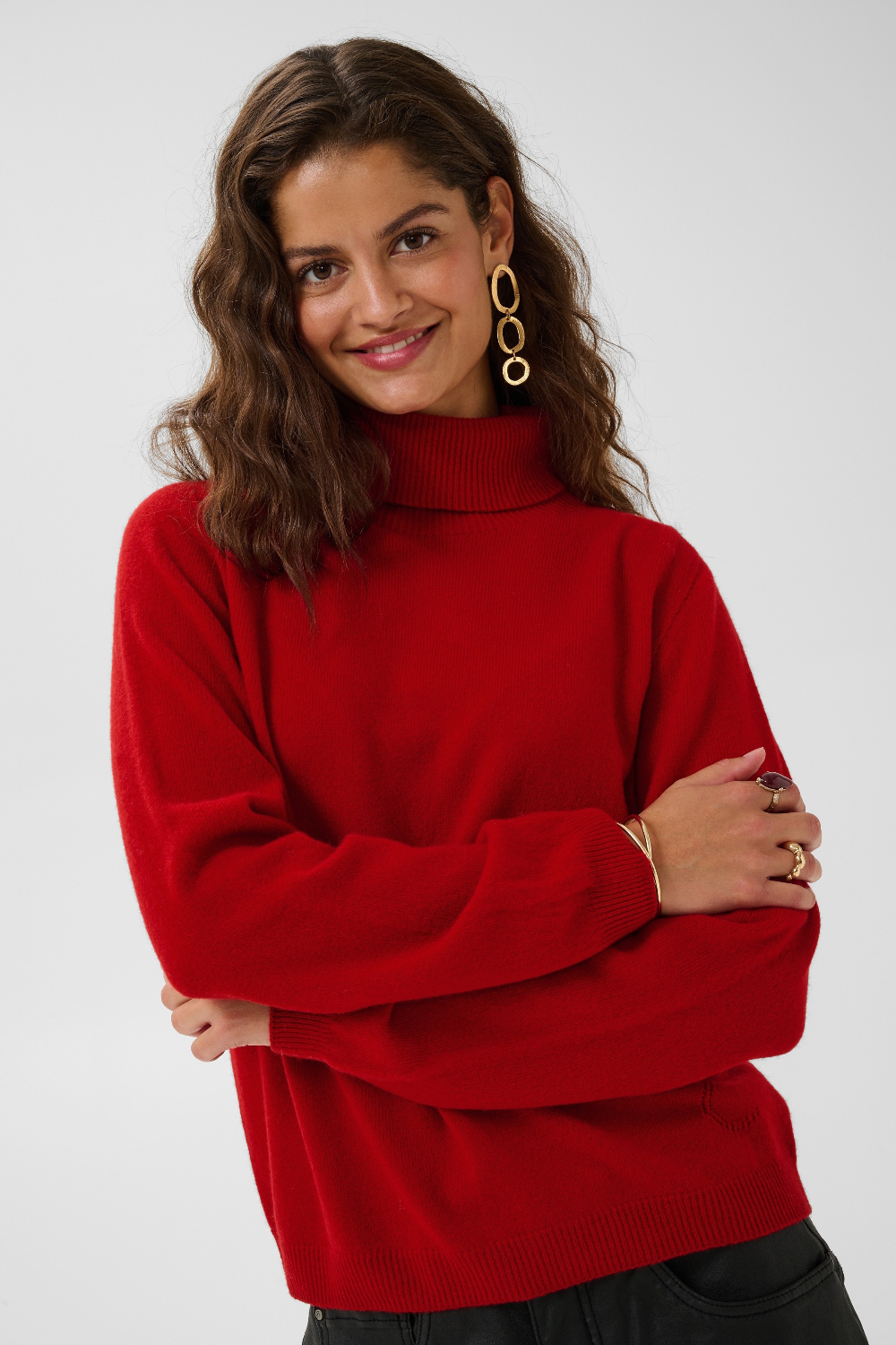 Woman modelling a red turtle neck sweater with black pants against a light backdrop.