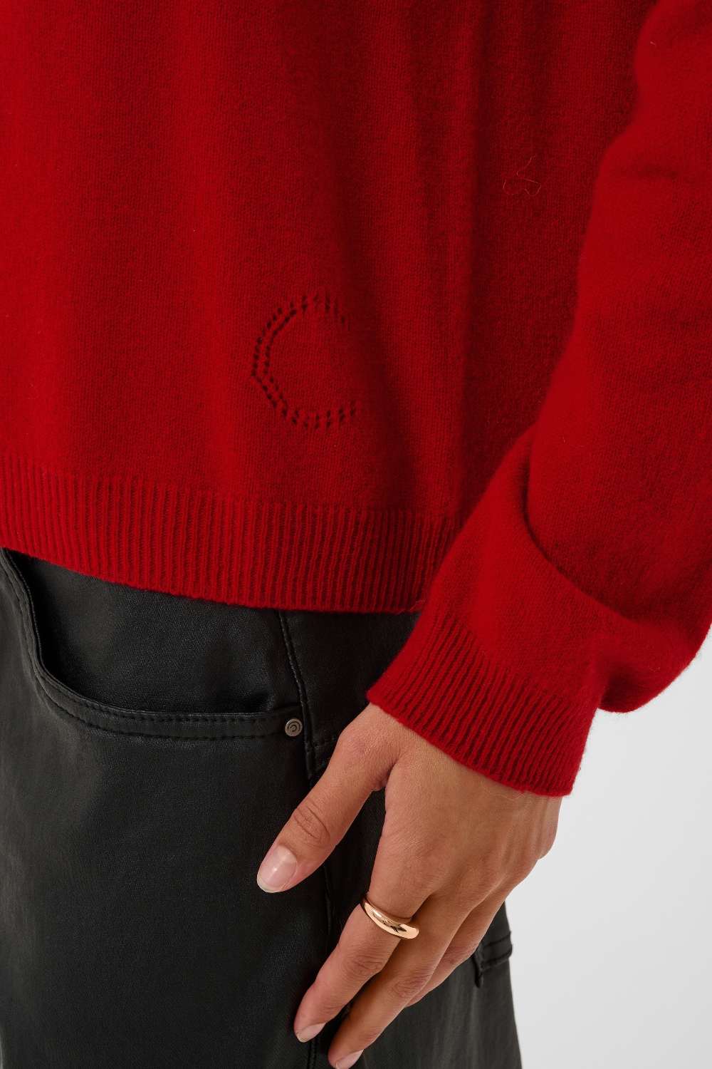 close up of a red turtle neck sweater with black pants against a light backdrop.