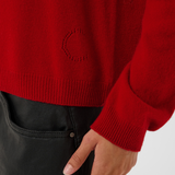 close up of a red turtle neck sweater with black pants against a light backdrop.