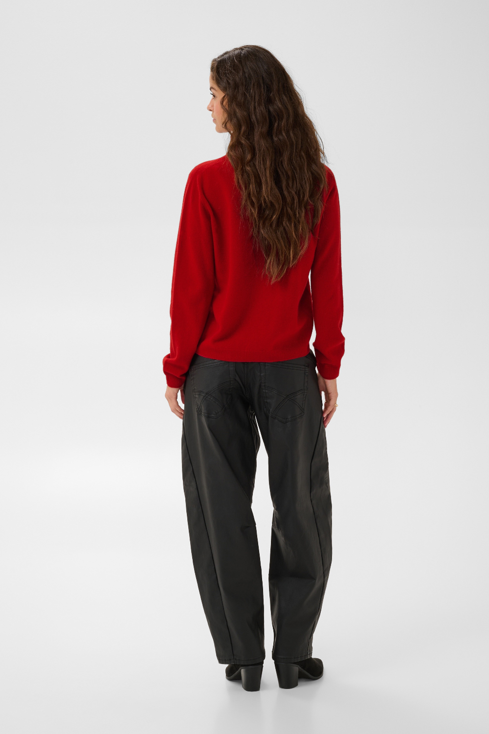 Woman, shown from behind, modelling a red turtle neck sweater with black pants and black boots against a light backdrop.