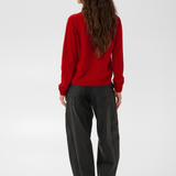 Woman, shown from behind, modelling a red turtle neck sweater with black pants and black boots against a light backdrop.