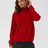 Woman modelling a red turtle neck sweater with black pants against a light backdrop.