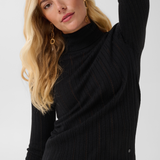 Woman modelling a black turtleneck with black pleather pants against a light backdrop.
