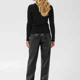 Woman, shown from behind, modelling a black turtleneck with black pleather pants and black boots against a light backdrop.