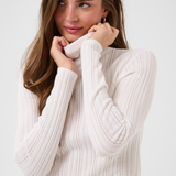 Woman modelling a cream turtleneck with beige corduroy pants against a light backdrop.
