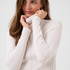 Woman modelling a cream turtleneck with beige corduroy pants against a light backdrop.