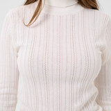 Close up of a woman modelling a cream turtleneck with beige corduroy pants against a light backdrop.
