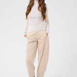 Woman modelling a cream turtleneck with beige corduroy pants and brown boots against a light backdrop.