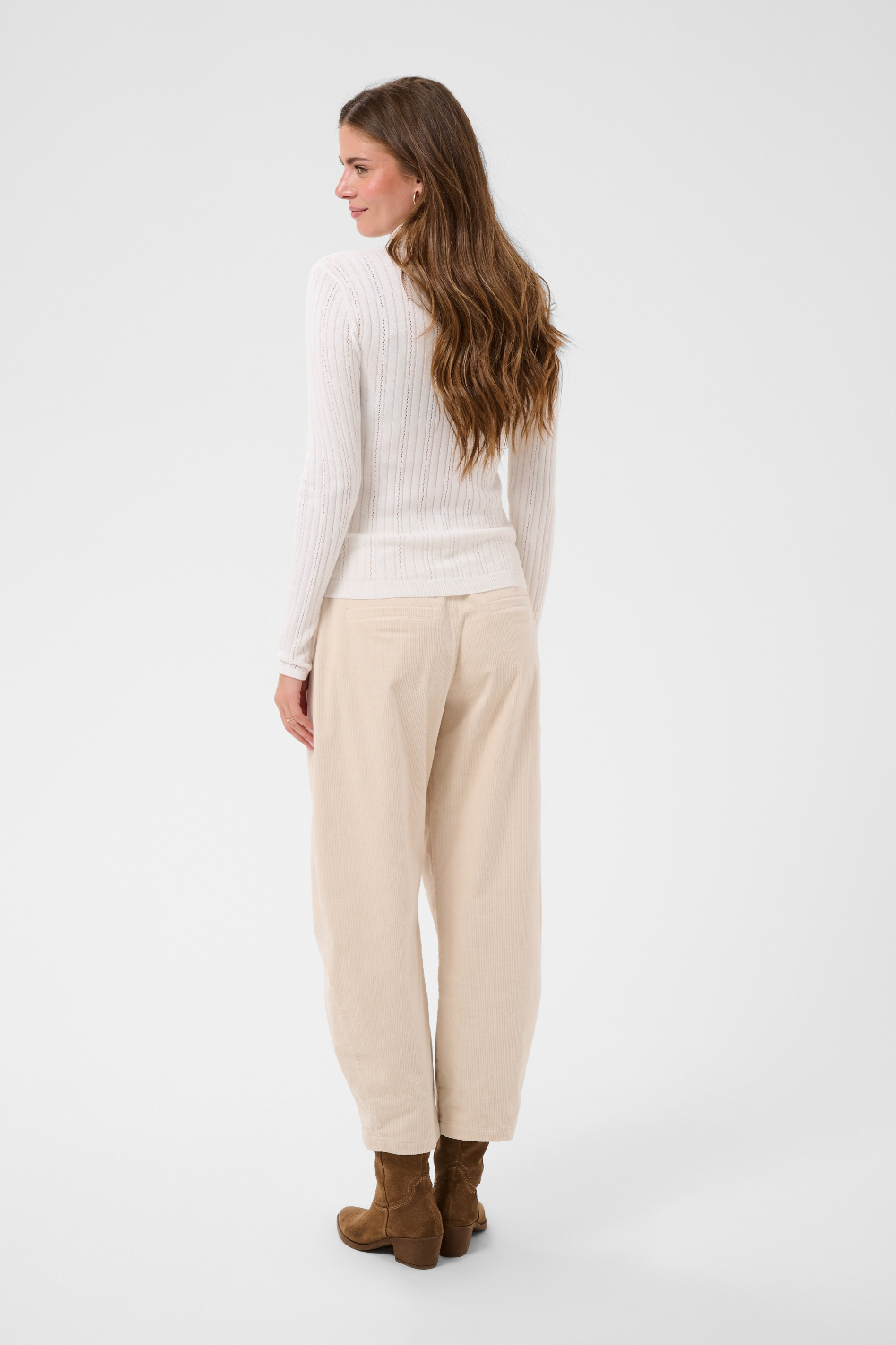 Woman, shown from the back, modelling a cream turtleneck with beige corduroy pants and brown boots against a light backdrop.