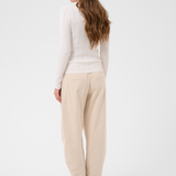 Woman, shown from the back, modelling a cream turtleneck with beige corduroy pants and brown boots against a light backdrop.
