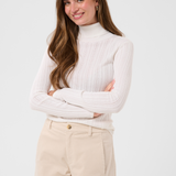 Woman modelling a cream turtleneck with beige corduroy pants against a light backdrop.