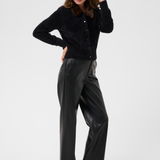Woman modelling a black button front cardigan, with an animal print collar, with black pants and black kitten heels photographed against a light backdrop.