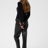 Woman, shown from behind, modelling a black sweater with black pants and black kitten heels photographed against a light backdrop.