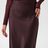 Close up of a woman modelling a deep wine coloured sateen skirt with a mesh top photographed against a light background.