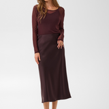 Woman modelling a deep wine coloured sateen skirt with a mesh top and black kitten heels photographed against a light background.