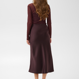 Woman, shown from the back, modelling a deep wine coloured sateen skirt with a mesh top and black kitten heels photographed against a light background.