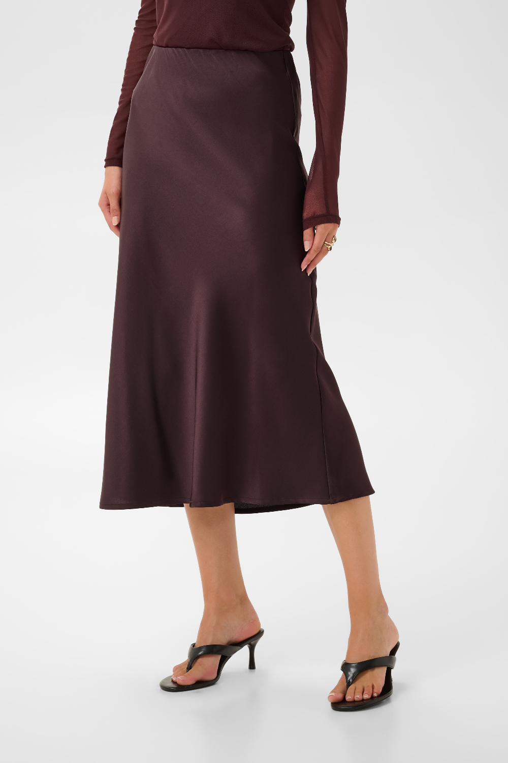 Woman modelling a deep wine coloured sateen skirt with a mesh top and black kitten heels photographed against a light background.