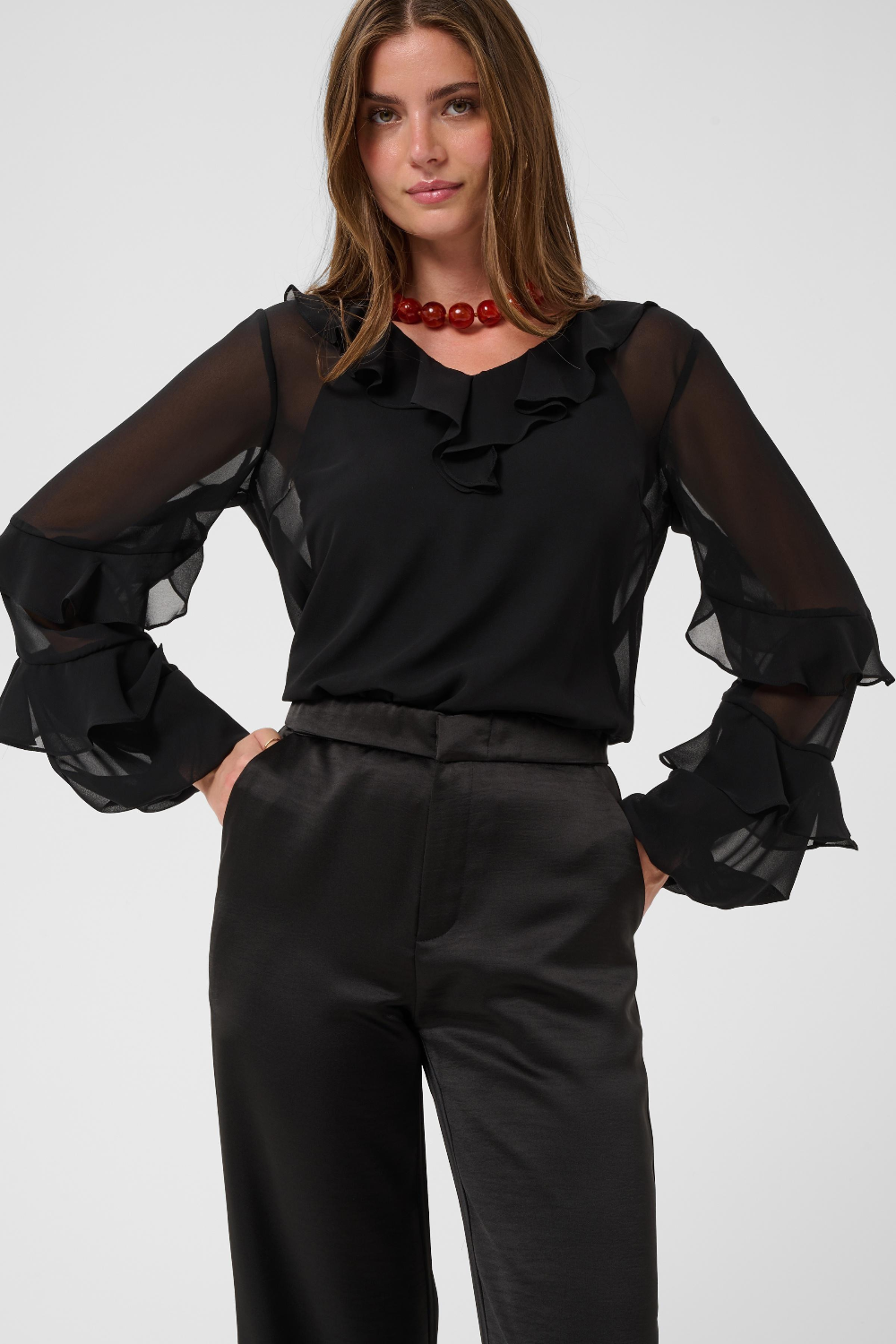 Woman modelling a sateen black pant a black blouse photographed against a light backdrop.