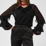 Woman modelling a sateen black pant a black blouse photographed against a light backdrop.
