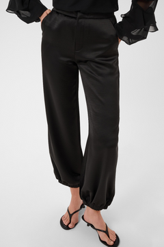 Woman modelling a sateen black pant with kitten heels and a black blouse photographed against a light backdrop.