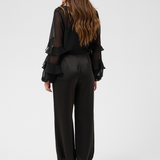 Woman, shown from behind, modelling a sateen black pant with kitten heels and a black blouse photographed against a light backdrop.