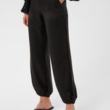 Woman modelling a sateen black pant with kitten heels and a black blouse photographed against a light backdrop.