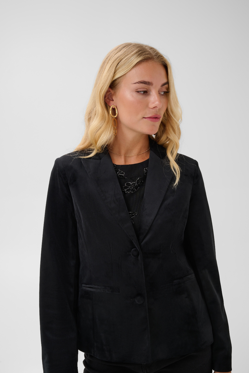 Woman modelling a black velour blazer with a sparkly black top and black pants photographed on a light background.
