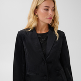 Woman modelling a black velour blazer with a sparkly black top and black pants photographed on a light background.