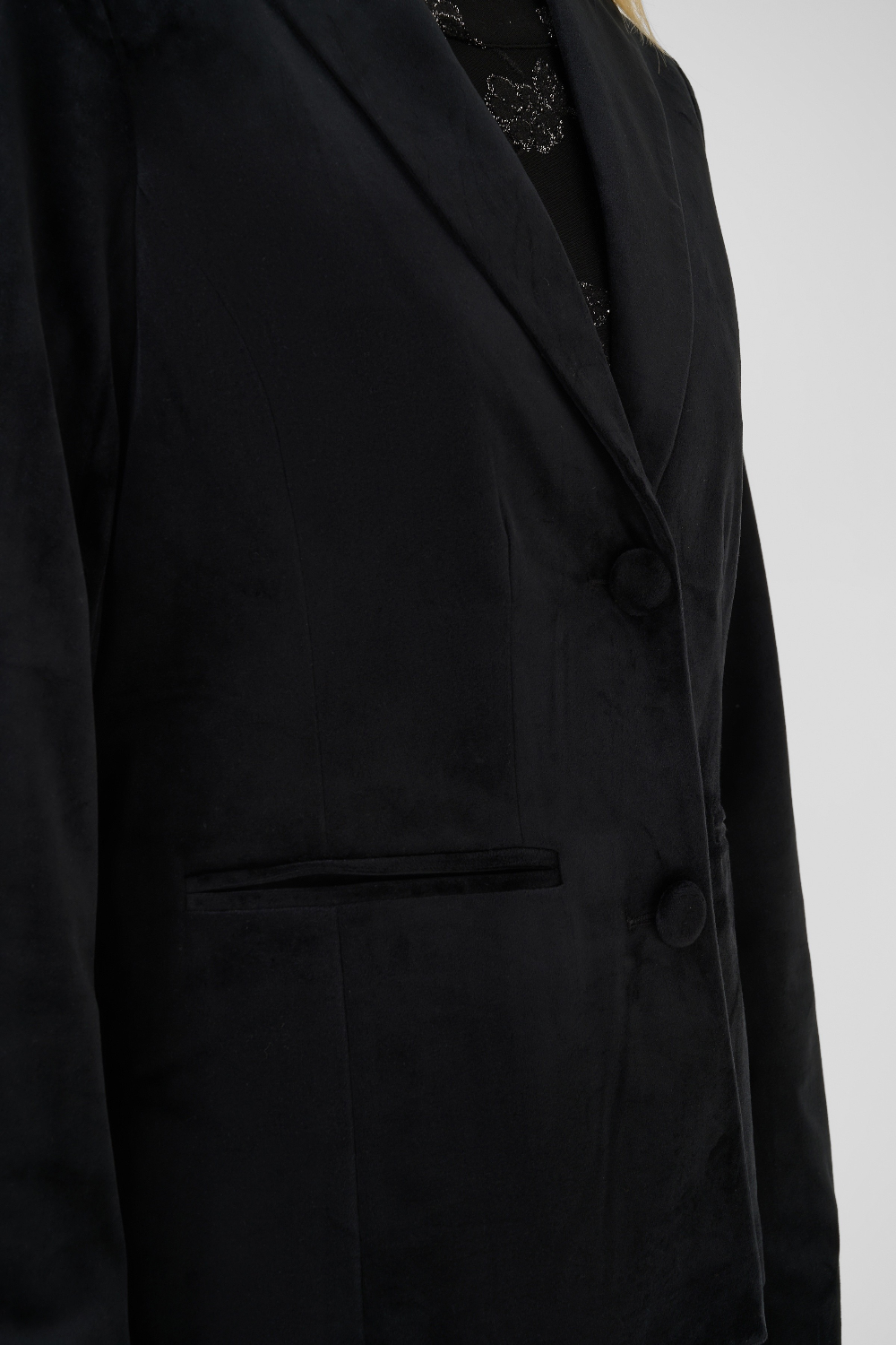 Close up of a woman modelling a black velour blazer with a sparkly black top photographed on a light background.