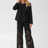 Woman modelling a black velour blazer with a sparkly black top, black pants and black heels photographed on a light background.