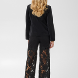 Woman, shown from the back, modelling a black velour blazer with black pants and black heels photographed on a light background.