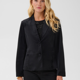 Woman modelling a black velour blazer with a sparkly black top and black pants photographed on a light background.