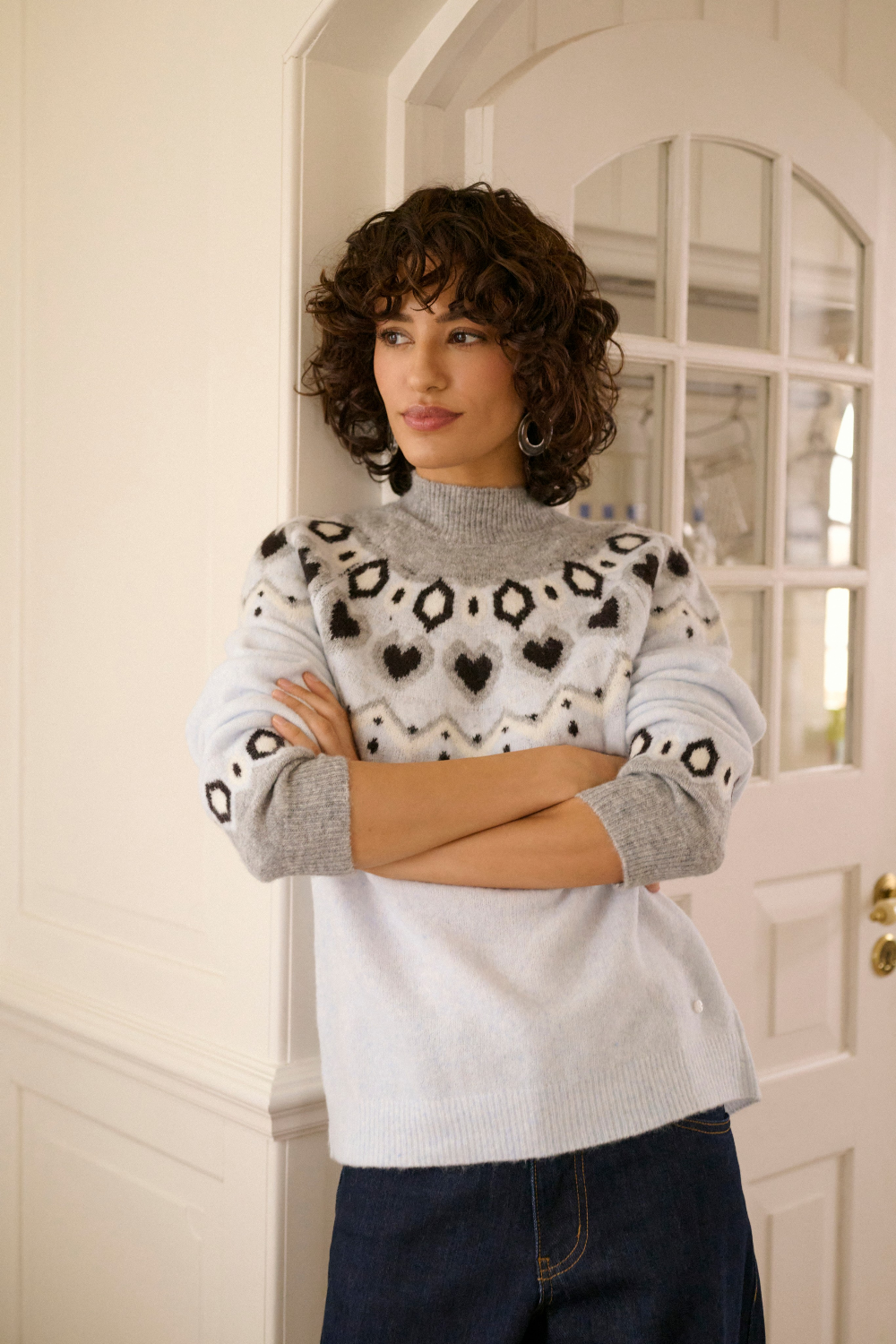 Woman modelling a fairisle inspired sweater with dark denim jeans photographed in an indoor setting.