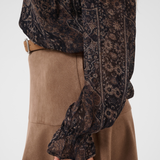 Close up of a woman modelling a printed brown v neck blouse with a tan skirt and belt photographed against a light background.