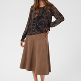 Woman modelling a printed brown v neck blouse with a tan skirt and shoes photographed against a light background.