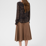 Woman modelling a printed brown v neck blouse with a tan skirt and shoes photographed against a light background.