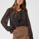 Woman modelling a printed brown v neck blouse with a tan skirt and belt photographed against a light background.