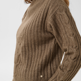 Close up of a woman modelling a brown 1/4 zip sweater with cream pants photographed against a light backdrop.