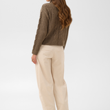 Woman, shown from behind, modelling a brown sweater with cream pants and brown boots photographed against a light backdrop.
