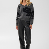 Woman modelling a grey v-neck sweater, with black accents, black pants and black boots against a light background.