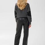 Woman, shown from behind, modelling a grey sweater, with black accents, black pants and black boots against a light background.