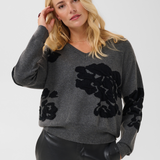 Woman modelling a grey v-neck sweater, with black accents, and black pants against a light background.